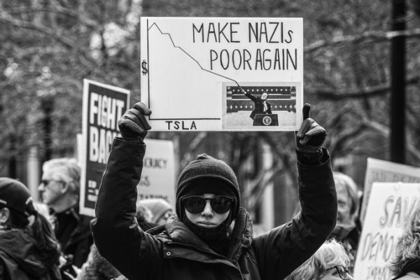 Black and white image of a protester holding a placard showing the graph of Tesla's dropping stock price coming from Space Karen's raised hand in a Nazi salute.  Text reads:

MAKE NAZIS POOR AGAIN