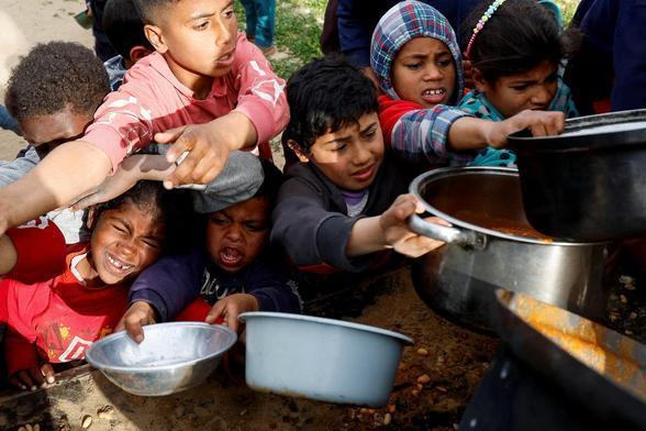 Palestinian children holding empty pots reach out for food.