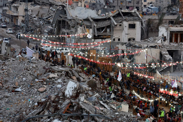 Lights and small red banners are strung around a long row of tables among the ruins.