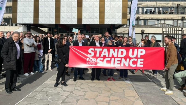 Protesters gather behind a huge red banner reading STAND UP FOR SCIENCE in Tours