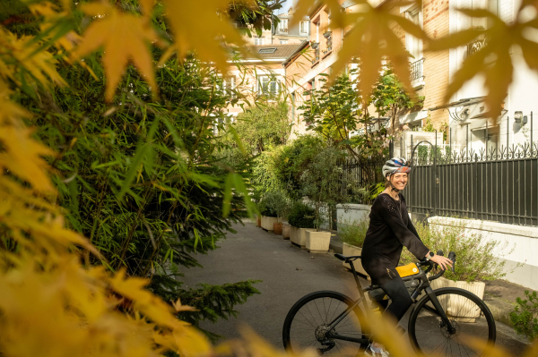 Photo d'une cycliste qu'on aperçoit entre des feuillages aux couleurs de l'automne