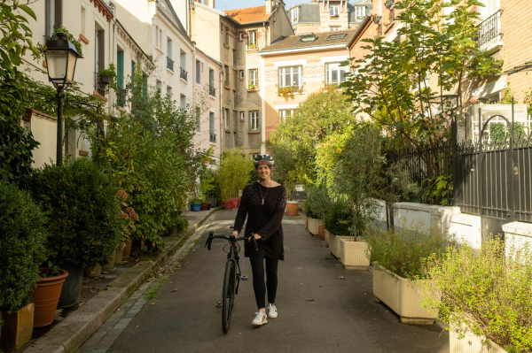 Photo d'une cycliste marchant à côté de son vélo dans une ruelle de la cité florale à Paris