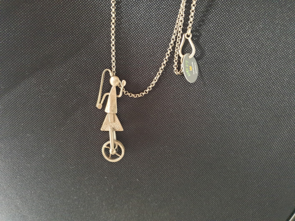 Collier en argent d'un personnage à queue de cheval sur un monocycle. 
Bijou fait à la main.