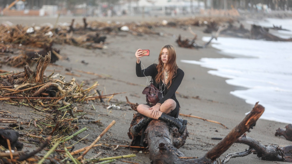 Eine Frau macht ein Selfie auf einem baustamm an einem Strand © IMAGO / CordonPress Foto: IMAGO / CordonPress