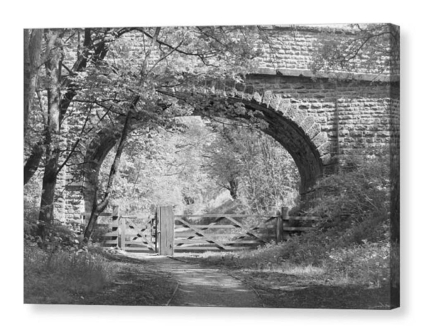 Black and white photograph showing a wooden gate on a footpath beneath a stone bridge.  The image is shown as a box canvas.