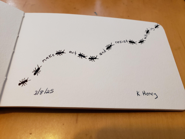 Hand drawn generative/procedural art in ink on an open page of my sketchbook. The abstract pattern looks like ants meandering across the page with words between them that read "make art and resist with joy".