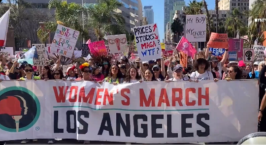 Huge crowd of protesters with placards, marching behind a banner reading WOMEN'S MARCH LOS ANGELES