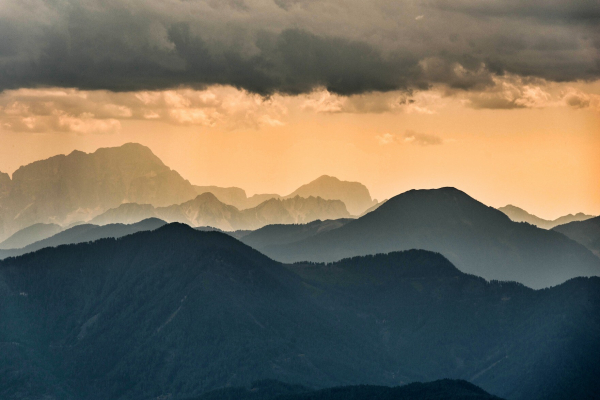 Blick über Berge beim Sonnenuntergang. Im oberen Teil des Bildes erkennt man dunkle Wolken. 