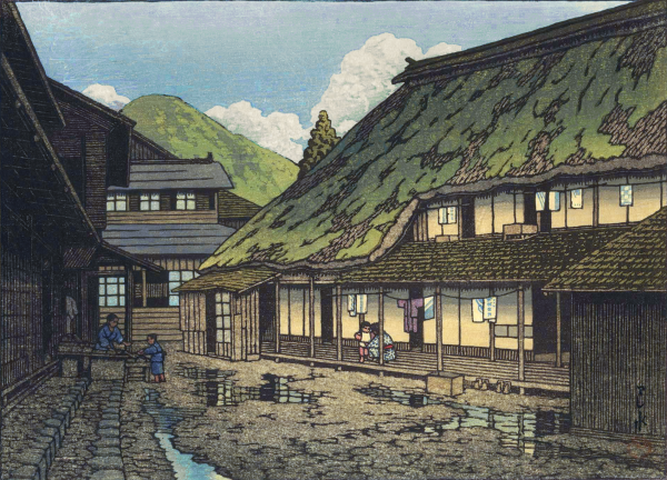 A view of a rural street in a mountain village at Iwate's Namari Onsen. There has been a recent rain, and puddles lie across the surface of the irregular road. Large houses stand on either side of the road and at the end of the street. At the house on the right, the sliding doors and windows are open, and laundry has been hung out to dry on the engawa, where a female figure is kneeling down, talking to a small child. Above, a patchwork of healthy-looking moss covers the steeply slanted thatched roof. At the house on the left, two children occupy the doorstep, one standing, one sitting. Beyond the village, tall green mountains flanked with puffy white clouds rise against a blue sky