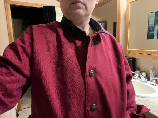 A photo of just the upper part of the coat, with interesting shadows. Most of my head is cut off, but the shadows show the drape of the fabric. The minimal rays of quilting on the front skip in and out of sight, and the smaller diamond pattern on the sleeves melts into the wrinkles. 